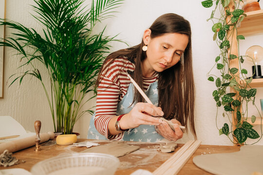 Woman carefully sculpting clay with detail tool in creative stud