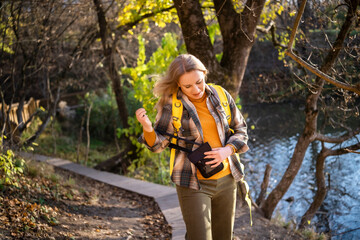 Woman adjusting crossbody bag while walking near lake in autumn park. Mindful nature walk supporting mental health and calm