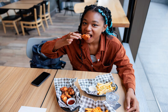 Young woman enjoys chicken wings and fries at restaurant.