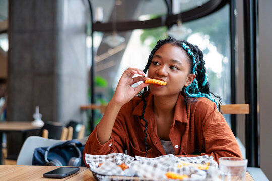 Woman with braids eats fries in a cafe.