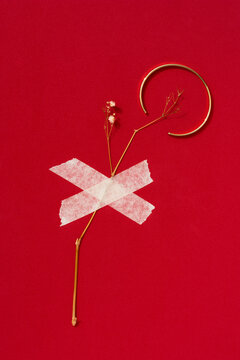 Gold bracelet and flower sticked with a tape on red background