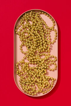 String of golden beads in a pink tray on red background
