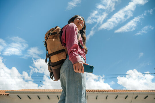  woman with backpack using phone under bright blue sky