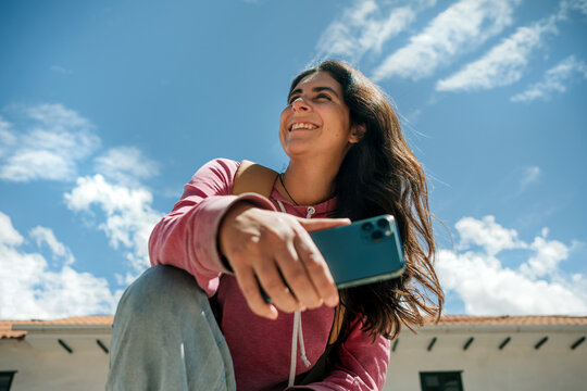 Smiling woman using phone under bright blue sky