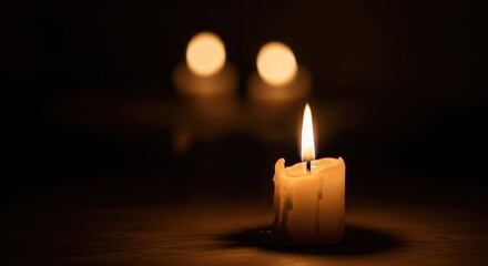A single lit candle with a blurred background of three other candles.