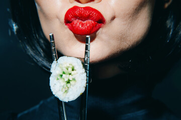 Stylish woman with red lips holding sushi with chopsticks, showcasing a modern, vibrant concept on a dark background for food lovers.