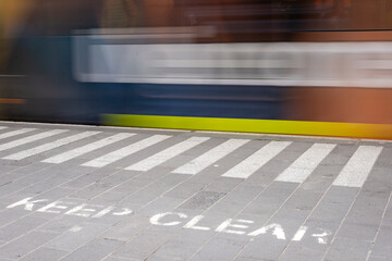 A Keep Clear notice in the forground with a train in motion in the background, train blurred