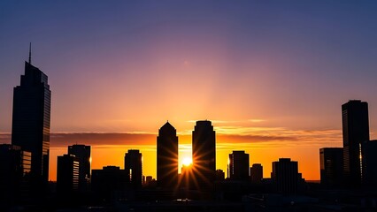 Cityscape at sunset with silhouetted skyscrapers against a vibrant orange and purple sky