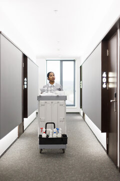 Focused latin maid going with cart and looking at room in hotel hall