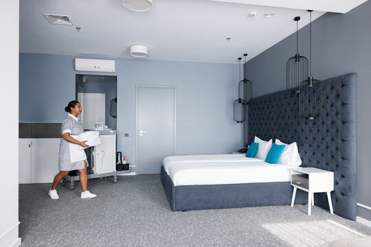 Side view of adult latin maid carrying towels on bed in hotel room