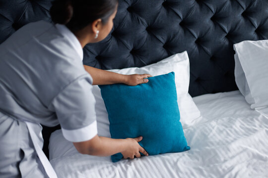 Partial view of maid fixing pillow on comfortable bed in hotel room
