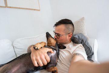 Man kissing dachshund on couch creating loving selfie moment