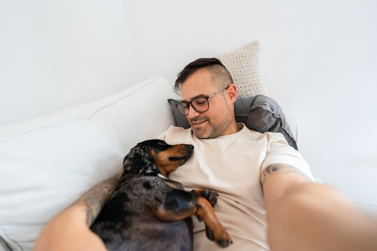 Man taking selfie with dachshund snuggling on couch