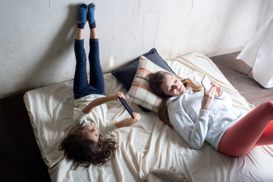 Mother and daughter looking at smartphones on bed at home