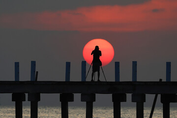 The silhouette of a photographer is taking pictures of the sunset on the bridge.