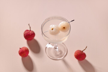 A stylish lychee cocktail with fruit garnish on a soft pink