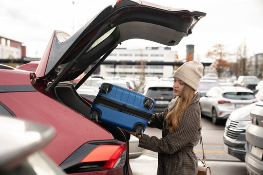 Woman Loading Blue Suitcase Into Car at Parking Lot