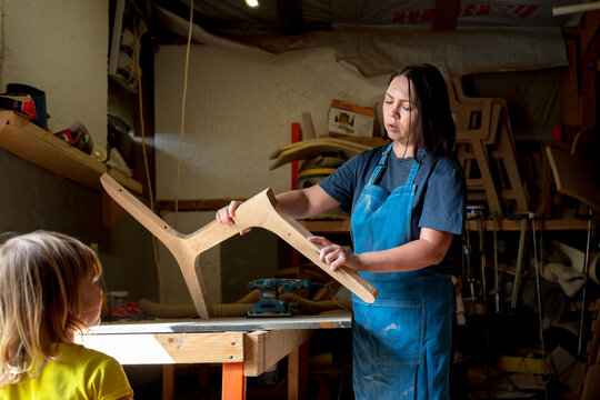 Woman in blue apron sanding or shaping wood in a workshop