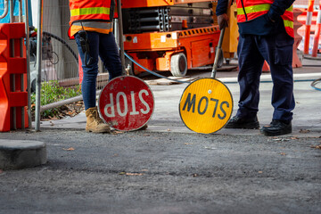 Two traffic controllers, one with a slow sign, one with a stop sign, work boots and safety vest construction site