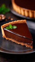 A glossy chocolate tart slice on a dark plate, with a mint leaf, warm browns, and a softly blurred background