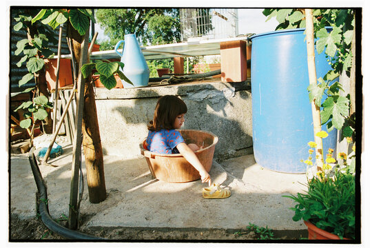 Child inside plastic tub beside blue barrel