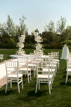 Outdoor Wedding Ceremony Setup with White Chairs and Floral Arch