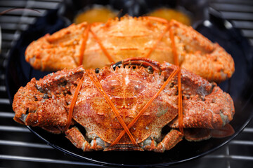 Steamed red crabs tied with rubber bands served on a black plate over a grill. Delicious fresh seafood delicacy ready for a meal, featuring vibrant orange shells and texture.