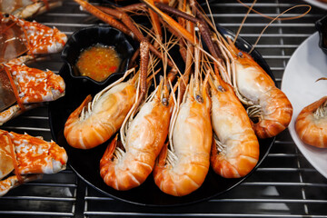 Fresh steamed giant river prawns served on a black plate with spicy Thai seafood dipping sauce. Delicious and healthy seafood delicacy with vibrant orange shells.