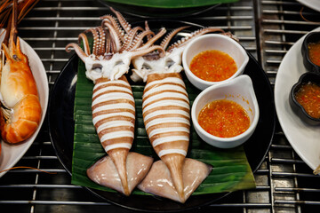 Fresh grilled squid with beautiful score marks served on banana leaf with spicy Thai seafood dipping sauce. Delicious street food delicacy ready to eat.