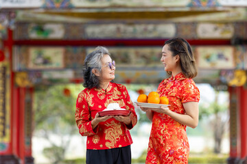 Obraz premium Asian woman with senior mother in red cheongsam qipao dress is offering food to ancestral god inside Chinese Buddhist temple during lunar new year for best wish blessing and good luck