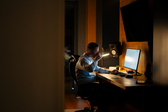 Man drinking coffee working late on computer at home office
