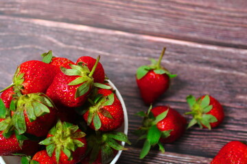 Fresh ripe strawberries overflowing from a white bowl on a dark rustic wooden table