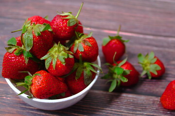 Fresh ripe strawberries overflowing from a white bowl on a dark rustic wooden table
