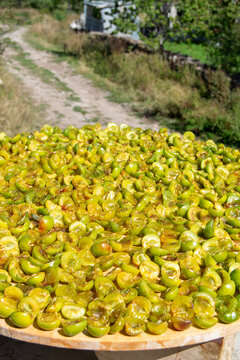 Cut green plums drying in the sun on a large round tray