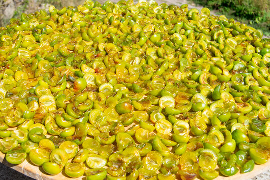 Cut green plums drying in the sun on a large round tray