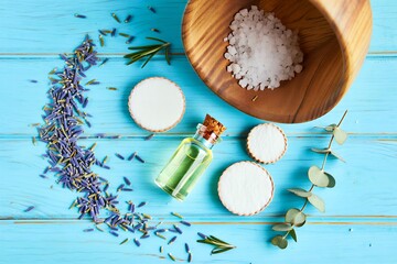 Relaxing spa treatment with lavender, essential oil, cotton pads, and sea salt on a blue wooden background, promoting wellness and tranquility for a serene escape