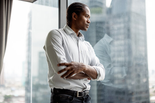 Professional Man Standing By Window Looking Out Over City Skyline 