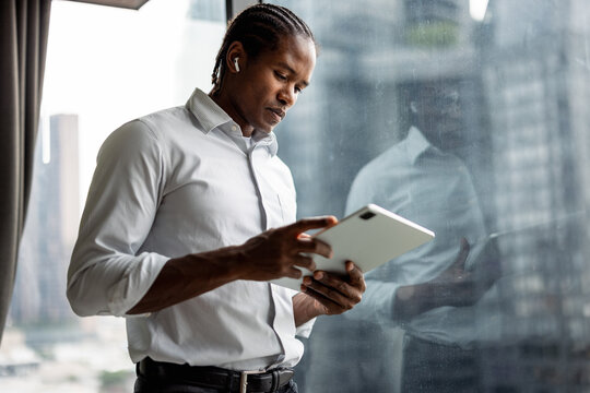 Businessman With Tablet and Earbuds Standing by a Window in an Office