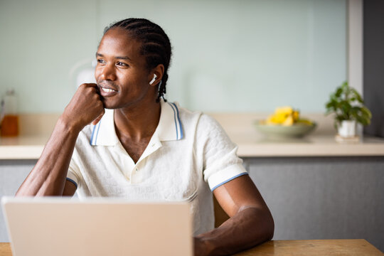 Thoughtful Man With AirPods Seated At A Desk In A Modern Apartment