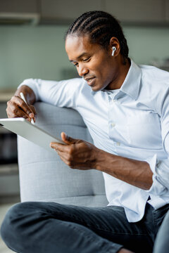 American Man Working on Tablet at Home with Wireless Earbuds