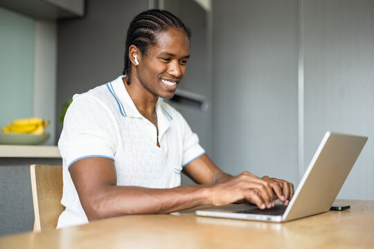 Smiling Man Wearing White Polo Working on Laptop with Earbuds 