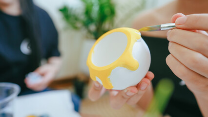Close-up of a person painting a ceramic cup with yellow acrylic paint during a DIY arts and crafts activity at home or art workshop.