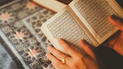 A close-up of a Muslim woman reading the Quran, holding the holy book with Arabic text on a patterned prayer mat, symbolizing Islamic faith, worship, and spirituality.