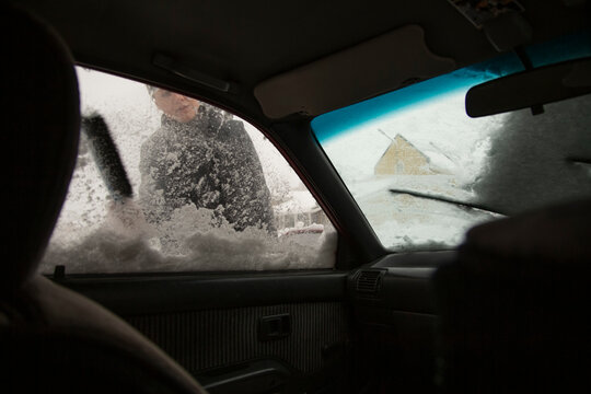 Person clearing snow from car windshield