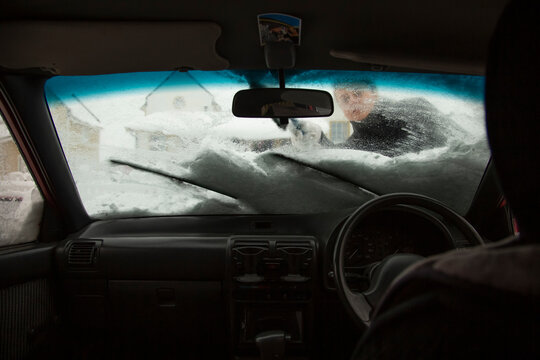 Man clearing snow from car windshield in winter