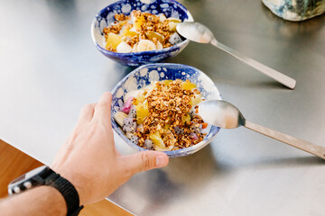 Hand taking a bowl of fruit prepared with granola and yogurt