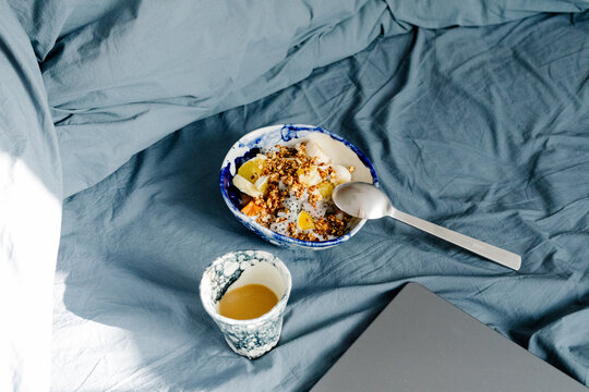 Bowl of fruit with placed on a bed next to a coffee and a laptop