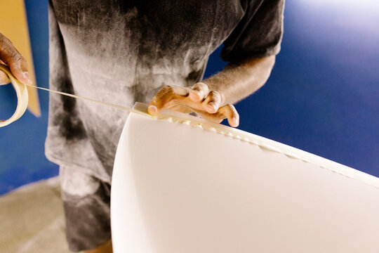 Unknown surfboard artisan applying masking tape on a new board