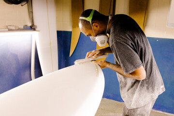 Surfboard maker smoothing and shaping the surface of a new board