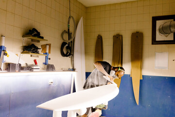 Artisan standing while hand-sanding a surfbroard in a workshop setting